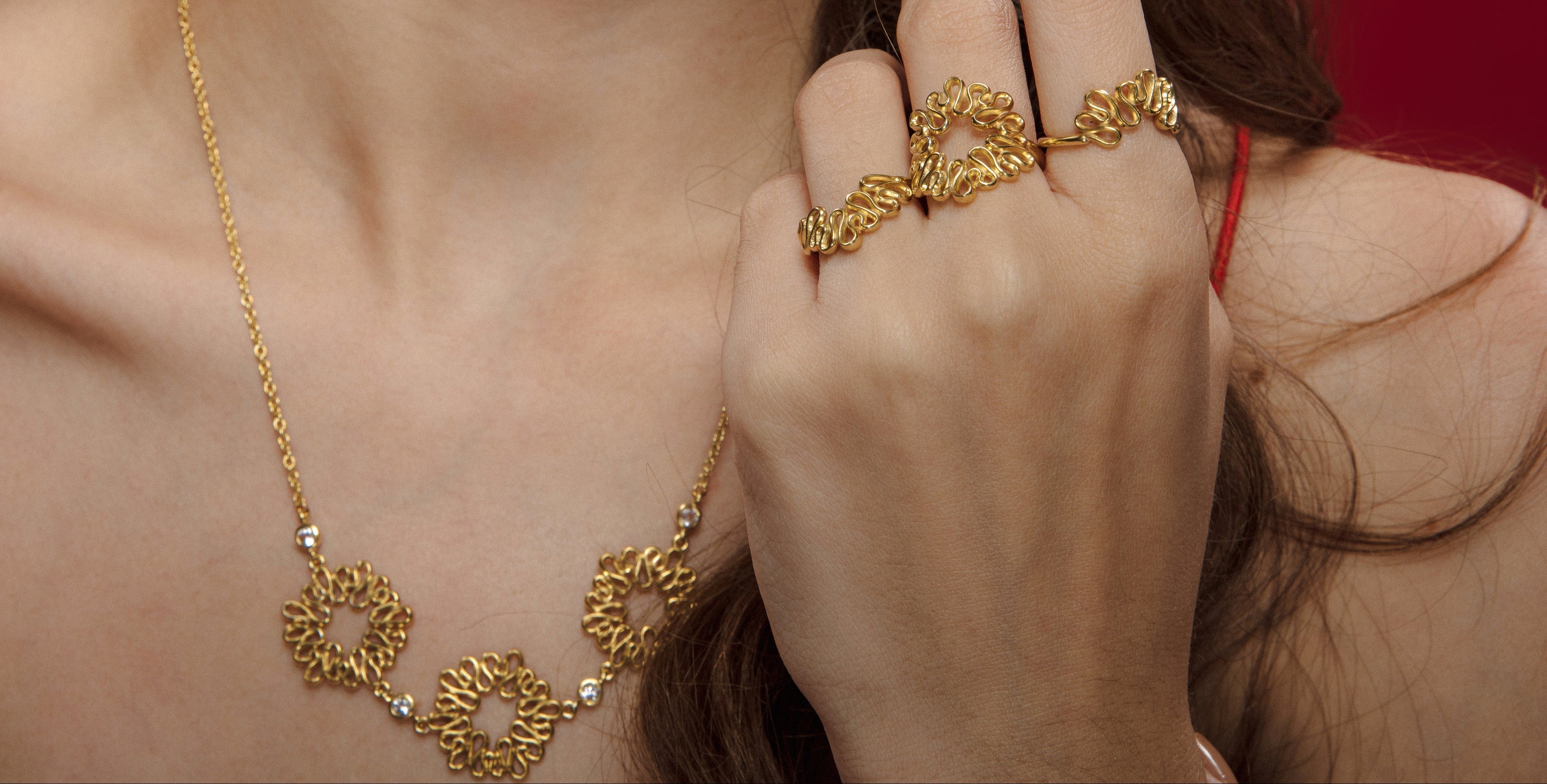 Woman wearing gold jewelry including a necklace, ring, and earrings against a red background